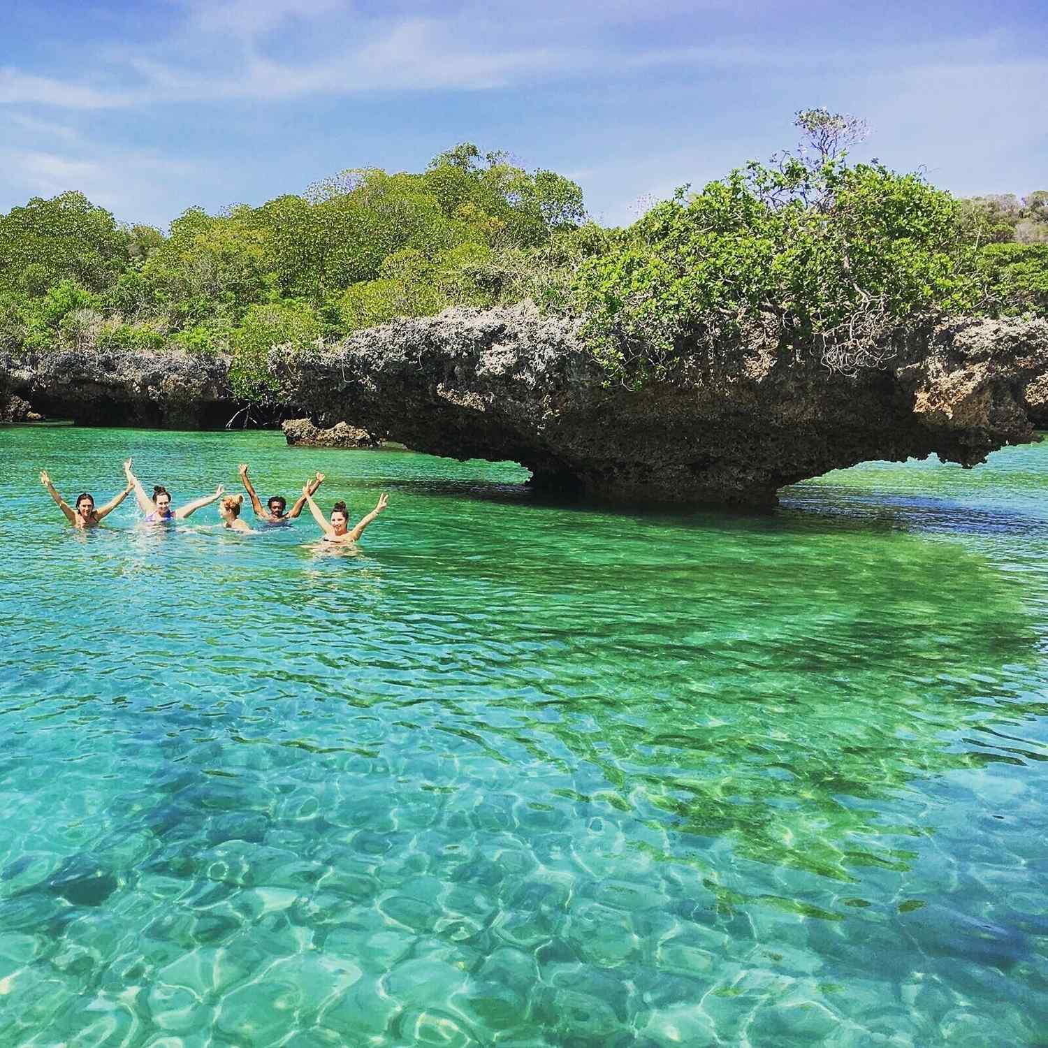 Guests swimming and celebrating in a clear turquoise lagoon beside a mushroom-shaped coral rock