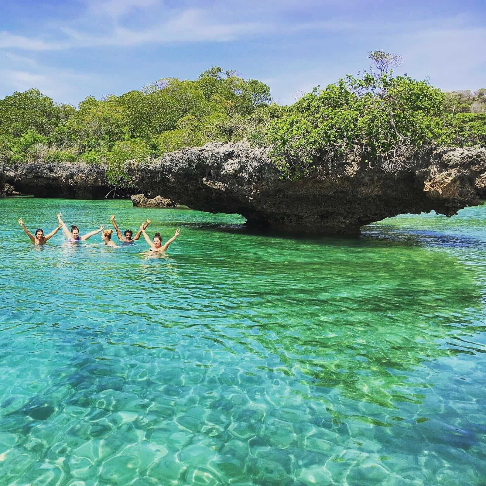 Group swimming beside a mushroom-shaped coral rock in a clear lagoon