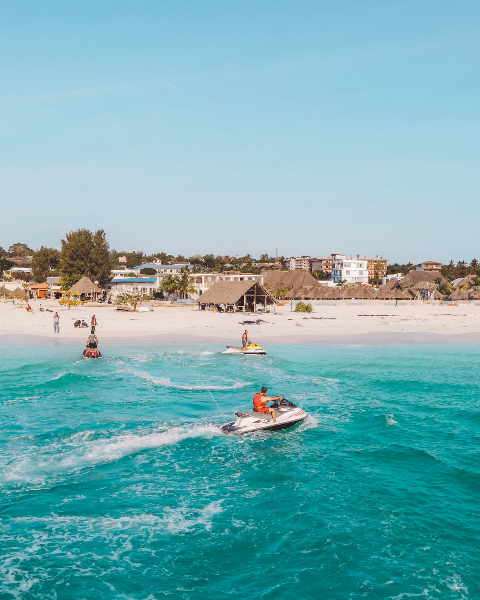 Jet skiers riding the waves off a white sand beach