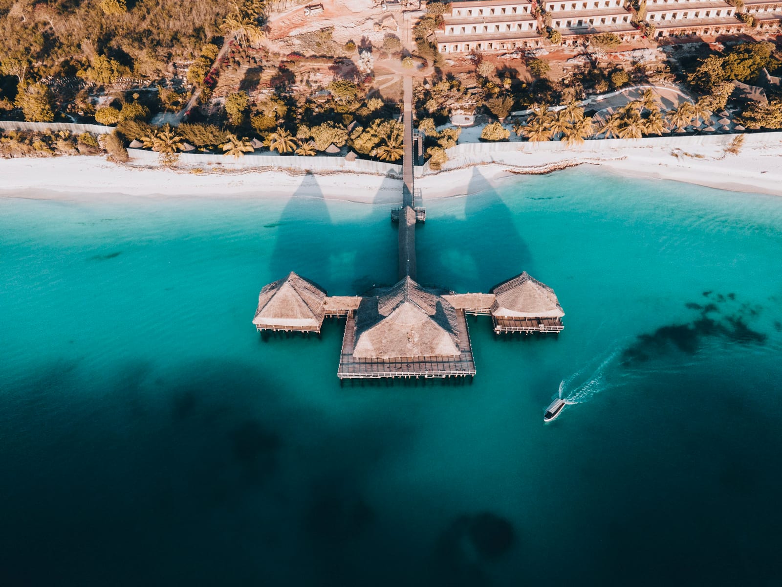 Aerial view of a thatched overwater restaurant with a boat passing by